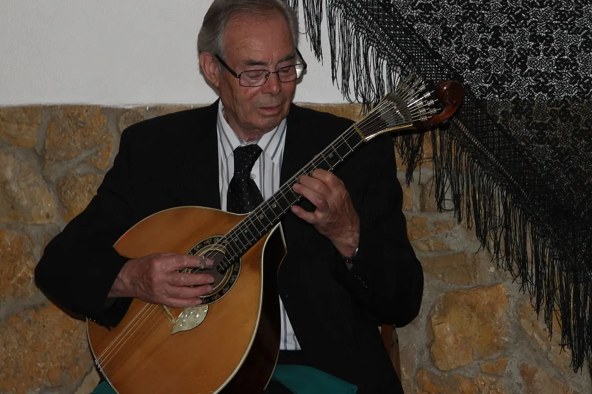 A guitarist in a dark waistcoat plays a pear-shaped Portuguese guitar with twelve strings in a Lisbon fado house