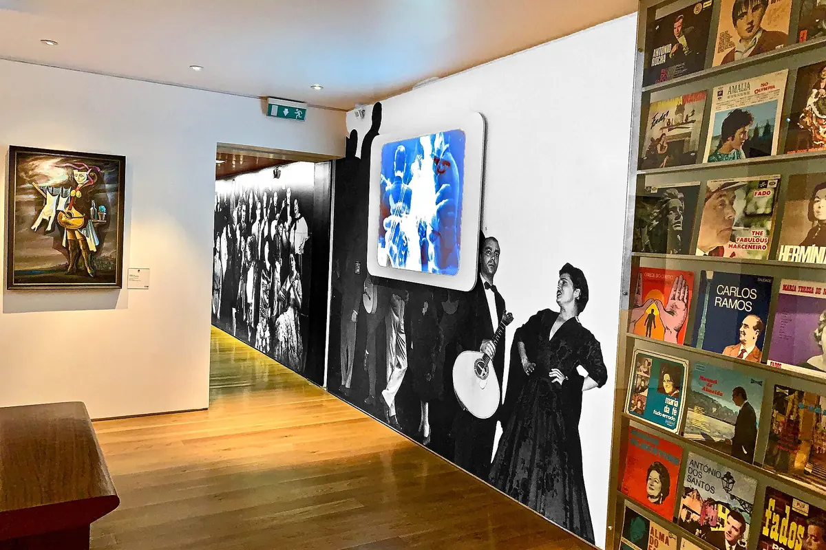 A corridor of the Museu do Fado with a wall of old fado record sleeves on one side and a large photograph of two fado musicians on the other