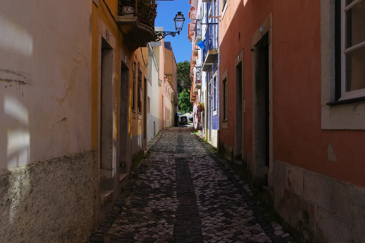 A narrow Alfama street in Lisbon where a battered wooden house on a stone wall rises above a small square with pigeons